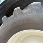 Close-up of a large tractor tire with dirt and scrapes; sidewall markings are visible on the tire surface.