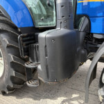 Close-up of a blue tractor showing a large treaded rear tire, blue body panel, and entry step.