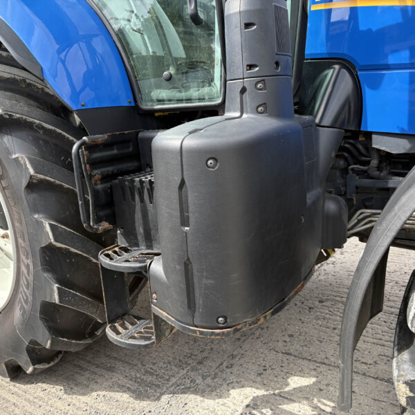 Close-up of a blue tractor showing a large treaded rear tire, blue body panel, and entry step.