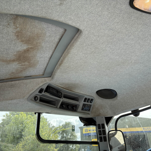 Interior of a truck cab ceiling with overhead console, switches, and a small orange dome light visible in the upper right corner, beige fabric headliner.