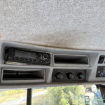 Dashboard of a truck cabin with a radio head unit and climate controls under a gray headliner, side window visible
