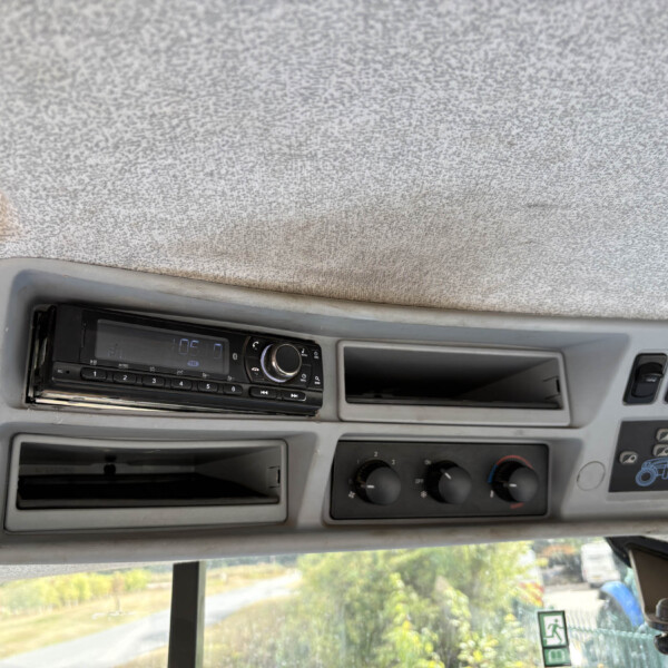 Dashboard of a truck cabin with a radio head unit and climate controls under a gray headliner, side window visible
