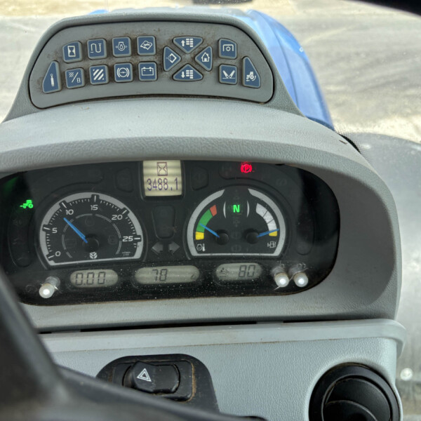 Close-up of a tractor cockpit: blue control icons array above the steering wheel, digital readout shows 3488.1 hours, and round gauges below.