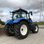 Blue agricultural tractor with large front tires and orange beacon on top, parked near power lines.