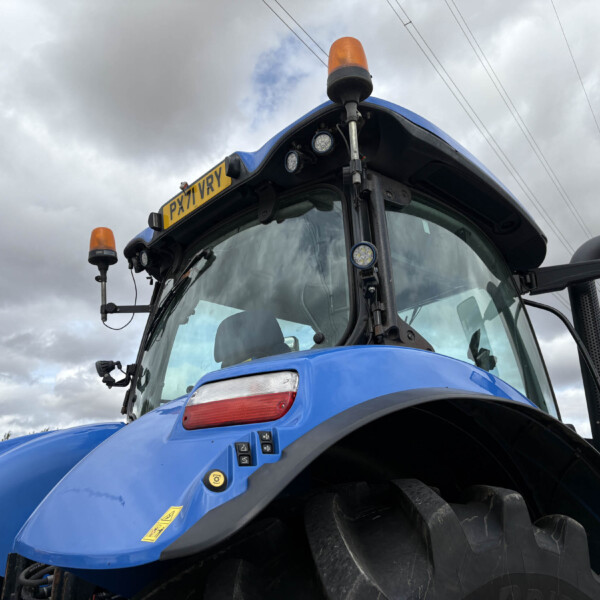 Front of a blue tractor with an orange warning beacon on top and the license plate PX71 VRY against a cloudy sky.