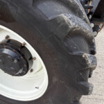 Close-up of a muddy tractor tire and white wheel hub with rusted lug nuts visible on the rim edge.