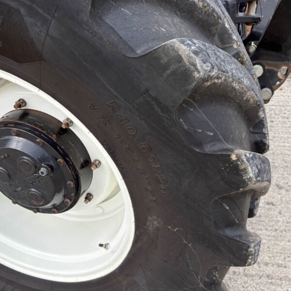 Close-up of a muddy tractor tire and white wheel hub with rusted lug nuts visible on the rim edge.