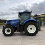 Blue New Holland tractor parked outside a New Holland Agriculture service building under a cloudy sky.
