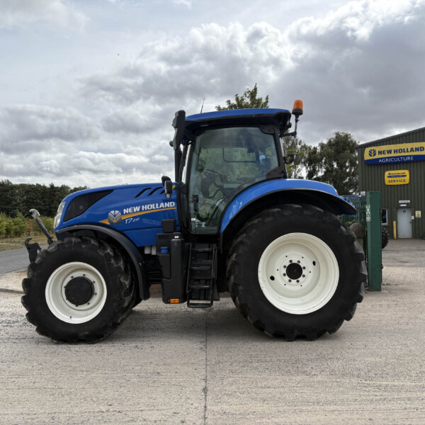 Blue New Holland tractor parked outside a New Holland Agriculture service building under a cloudy sky.