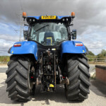 Front view of a blue tractor with oversized rear tires and orange warning lights, license plate PX71 VRY, under a cloudy sky at a rural site.