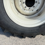 Close-up of a dirty vehicle wheel with a white rim and black tire, showing lug nuts and dirt buildup around the hub