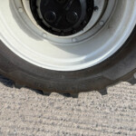 Close-up of a car tire mounted on a white wheel with dirt around the rim and on the ground nearby.