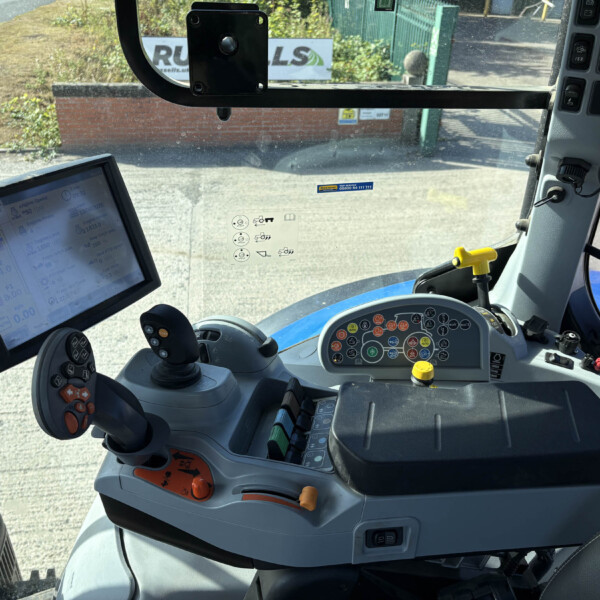 Inside a tractor cab showing a touchscreen display, joystick controls, and a full panel of buttons and levers nearby.