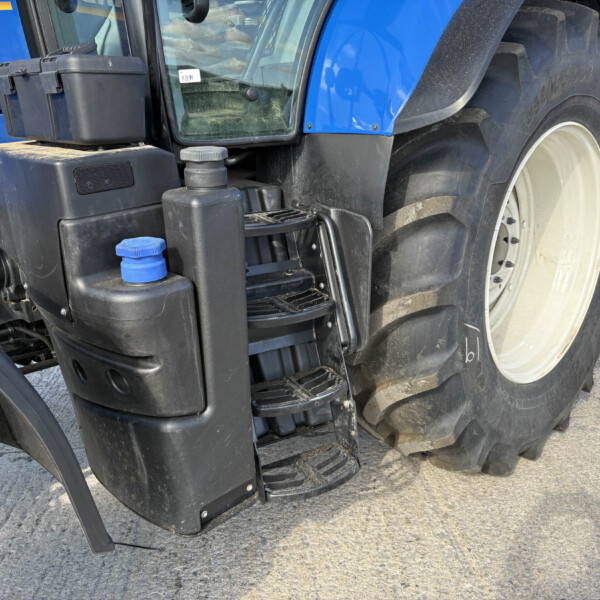 Close-up of a blue tractor's front left, showing steps, hydraulic reservoir, and a large tire with mud.