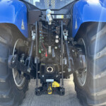 Rear view of a blue tractor showing its hydraulic control levers and wiring between large rear tires