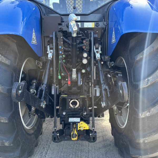 Rear view of a blue tractor showing its hydraulic control levers and wiring between large rear tires
