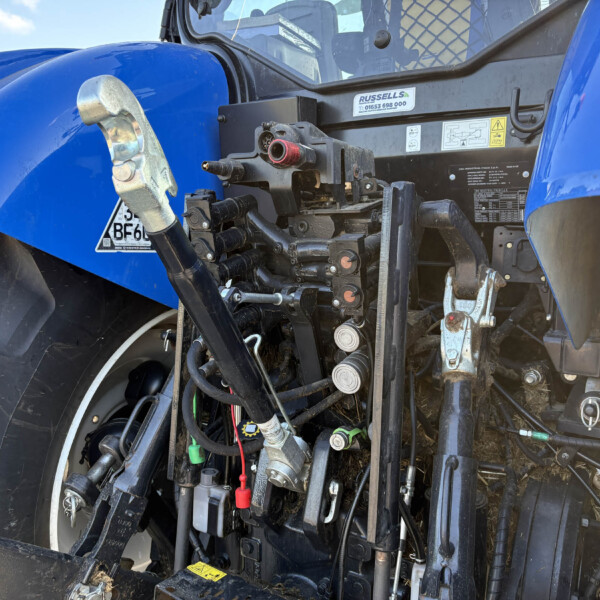 Close-up of a blue tractor front with hydraulic hoses, valves, and control levers exposed near the wheel.