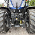 Front view of a blue New Holland tractor with large dual tires, front hitch and headlights visible between oversized tires