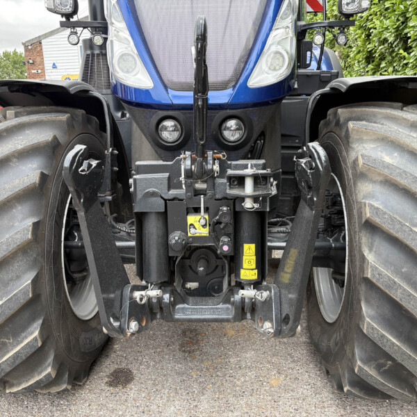 Front view of a blue New Holland tractor with large dual tires, front hitch and headlights visible between oversized tires