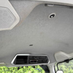 Interior view of a vehicle cabin ceiling with a speaker, overhead console, and fabric headliner.