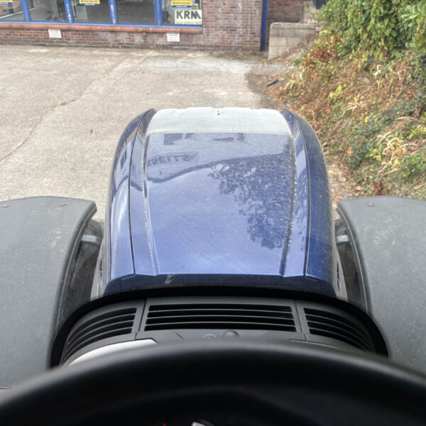 Driver's-eye view from inside a blue vehicle looking over the hood at a brick building and greenery outside.