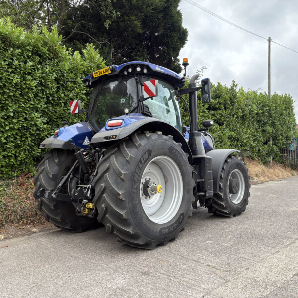 Blue tractor parked along a hedge on a residential street with overcast sky in the background.