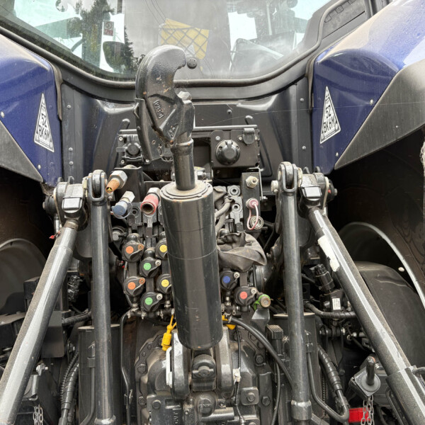 Close-up of a tractor’s front chassis with hydraulic levers, hoses, and linkage components visible at center.