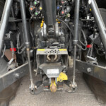 Close-up of a hydraulic control manifold with colored valve caps and hoses inside heavy machinery chassis.
