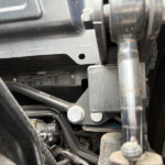 Close-up of a vehicle engine bay showing a metal bracket, hoses, and a data plate with specifications.
