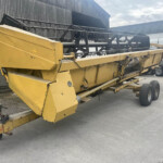 Large yellow industrial conveyor or auger on wheels, parked beside a gray corrugated building.