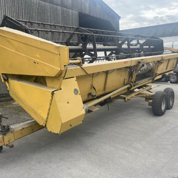 Large yellow industrial conveyor or auger on wheels, parked beside a gray corrugated building.