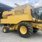 New Holland TF78 large yellow agricultural machine with oversized tires parked beside a shed.