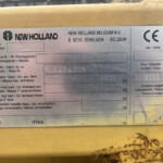 Identification plate on yellow machinery showing New Holland logo, Belgium address, and CE mark