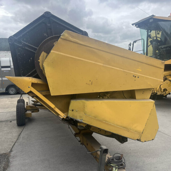 Yellow industrial machinery with a tilted conveyor/chute, cabin on the right, parked on a concrete surface under a cloudy sky.