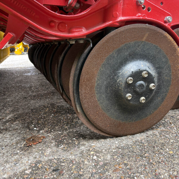 Close-up of large rusty steel rollers beneath a red agricultural implement on a gravel surface.