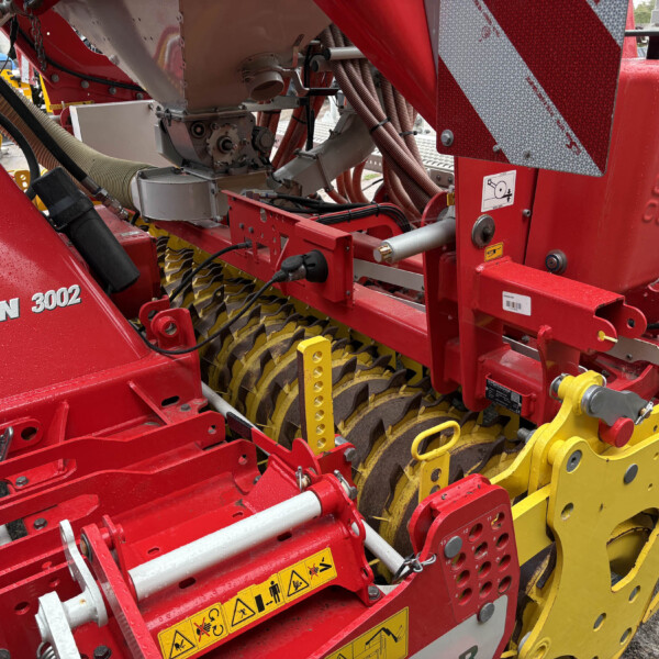Close-up of red agricultural machinery showing hydraulic hoses, metal components, and yellow-inserted wheels with safety decals nearby red frame.