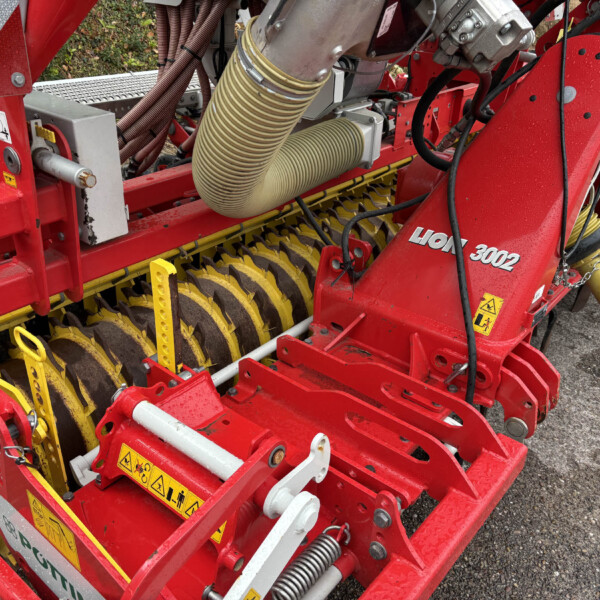 Close-up of a red agricultural implement showing yellow rotating discs, hoses, and warning labels.