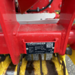Close-up of red agricultural equipment with a black data plate showing model and serial number and a QR code on the label.