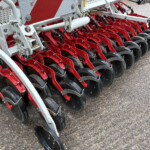 Close-up of a red agricultural planter with multiple disc coulters and a gray frame.