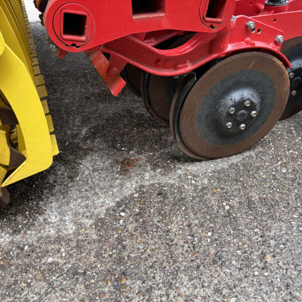 Close-up of a red construction machine’s frame with brown steel wheels beside a yellow attachment on an asphalt surface.