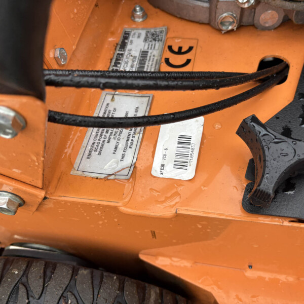 Close-up of orange industrial machinery with warning and barcode labels and black hoses crossing the surface.