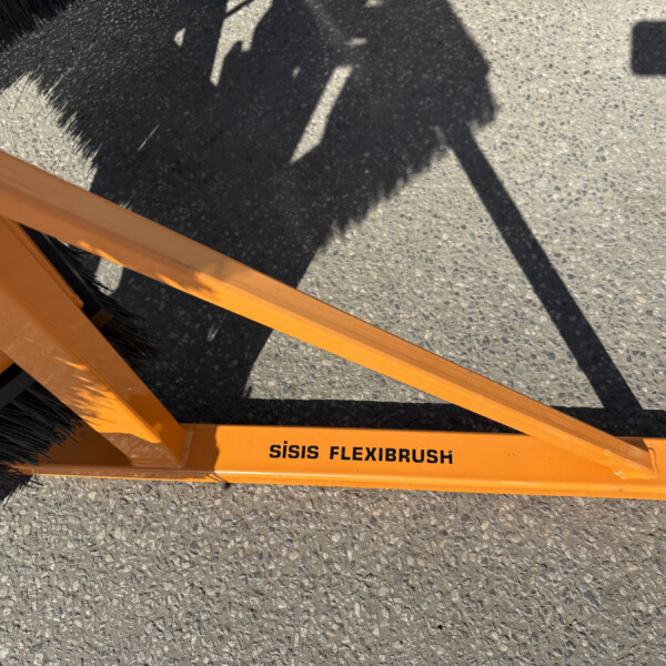 Close-up of an orange ISISIS FlexiBrush attachment on the ground, showing black bristles and stamped text along the beam.