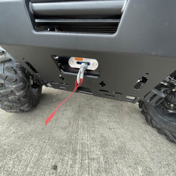 Front bumper of a rugged off-road vehicle with a winch and red tow strap attached, large tread tire visible on the left.