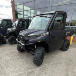 Three black off-road utility vehicles with oversized tires parked outside a glass-fronted building, likely a dealership showroom.