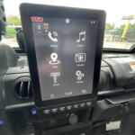 Vehicle infotainment touchscreen displaying apps (Phone, Music, Map, Camera, Settings) inside a car cabin.