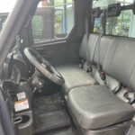 Interior of a black truck cab showing the driver's seat and a bench seat, steering wheel, and large side window; visible warning sticker near the pedals and a dirty floor mat.