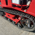 Close-up of a red tracked machine's undercarriage showing the black rubber track and wheels behind the red frame.