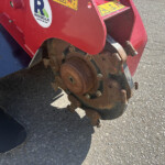 Close-up of a rusted gear assembly on a red agricultural implement with warning stickers