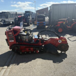 Red farm machinery and trailers parked in an outdoor equipment yard, with a blue sky and clouds above.