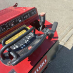 Close-up of a red industrial control panel with safety icons and a joystick on the machine's body